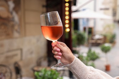 Woman holding glass of rose wine outdoors, closeup