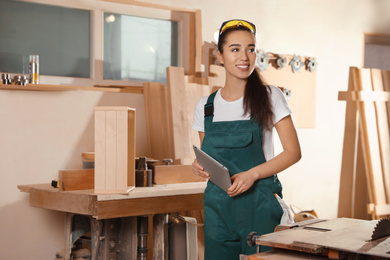 Photo of Professional carpenter in uniform with tablet near workbench