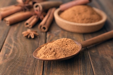 Spoon with aromatic cinnamon powder on wooden background