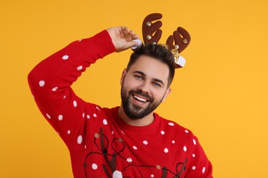 Photo of Happy young man in Christmas sweater and reindeer headband on orange background