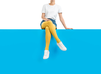 Woman wearing yellow tights and stylish shoes sitting on color background, closeup