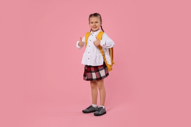 Happy schoolgirl with backpack on pink background