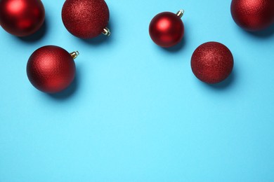 Photo of Red Christmas balls on light blue background, top view. Space for text