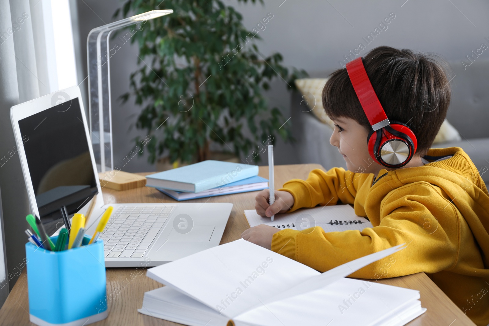 Photo of Cute little boy with modern laptop studying online at home. E-learning