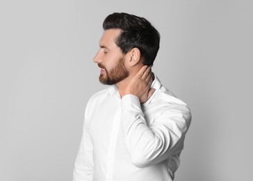 Photo of Man suffering from pain in his neck on light background. Arthritis symptoms