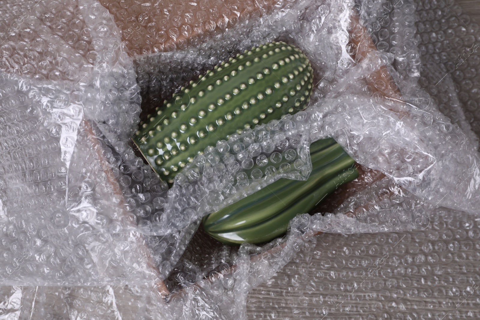 Photo of Ceramic cacti with bubble wrap in cardboard box on wooden table, top view