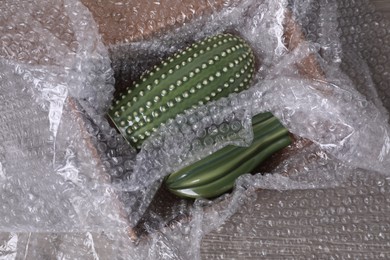 Ceramic cacti with bubble wrap in cardboard box on wooden table, top view