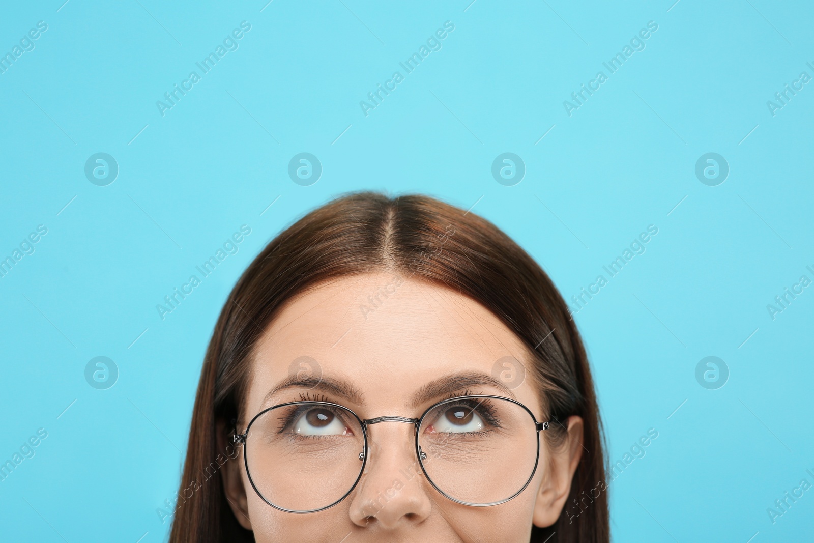 Photo of Woman in stylish eyeglasses looking up on light blue background, closeup