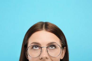 Woman in stylish eyeglasses looking up on light blue background, closeup