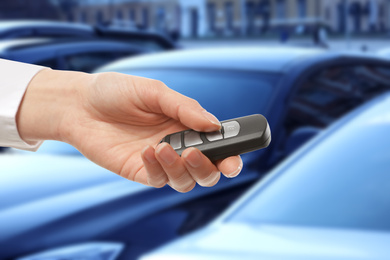 Image of Car buying. Woman holding key against blurred automobiles, closeup