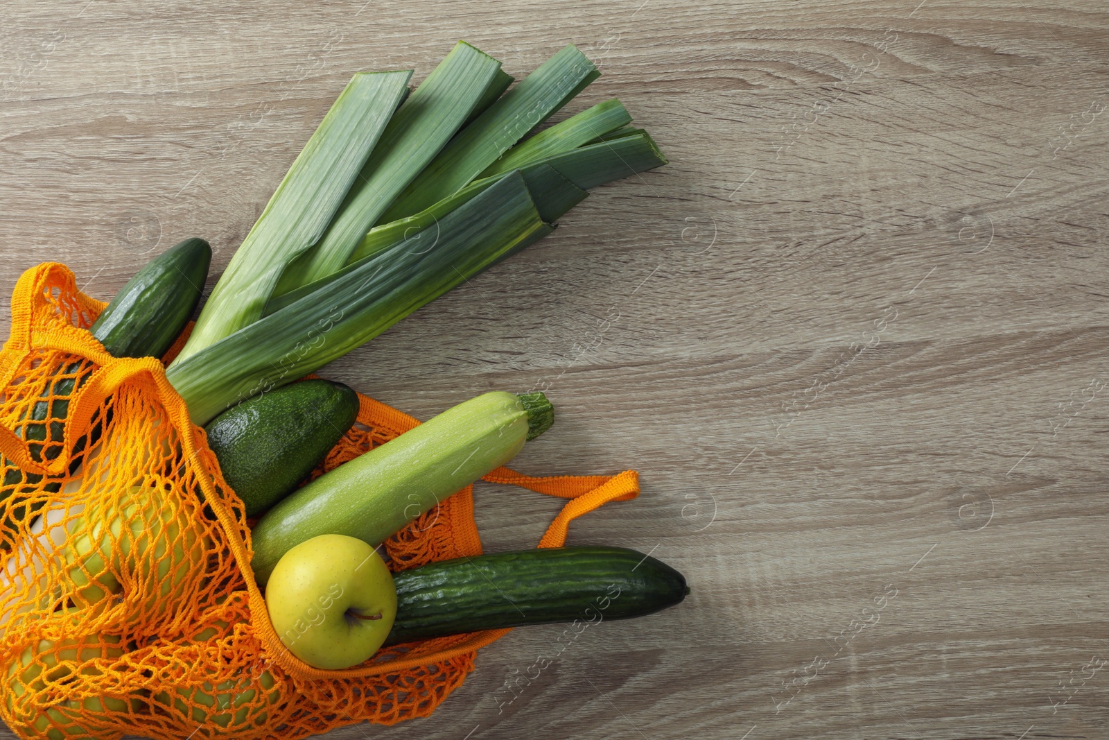 Photo of Net bag with vegetables and fruits on wooden table, top view. Space for text