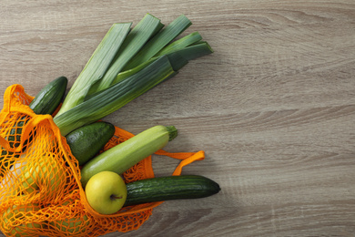 Net bag with vegetables and fruits on wooden table, top view. Space for text