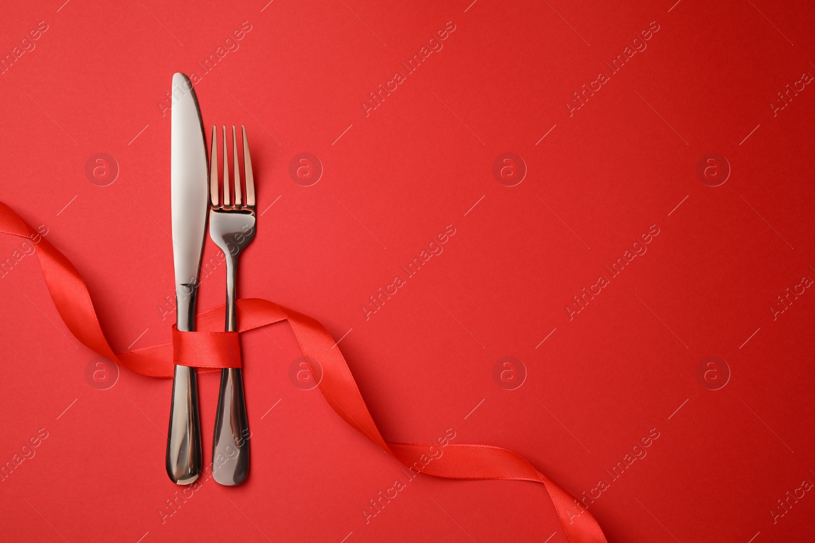 Photo of Cutlery set with ribbon on red background, flat lay and space for text. Romantic table setting