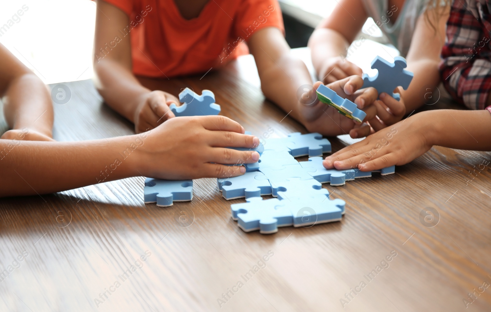 Photo of Little children playing with puzzle at table, focus on hands. Unity concept