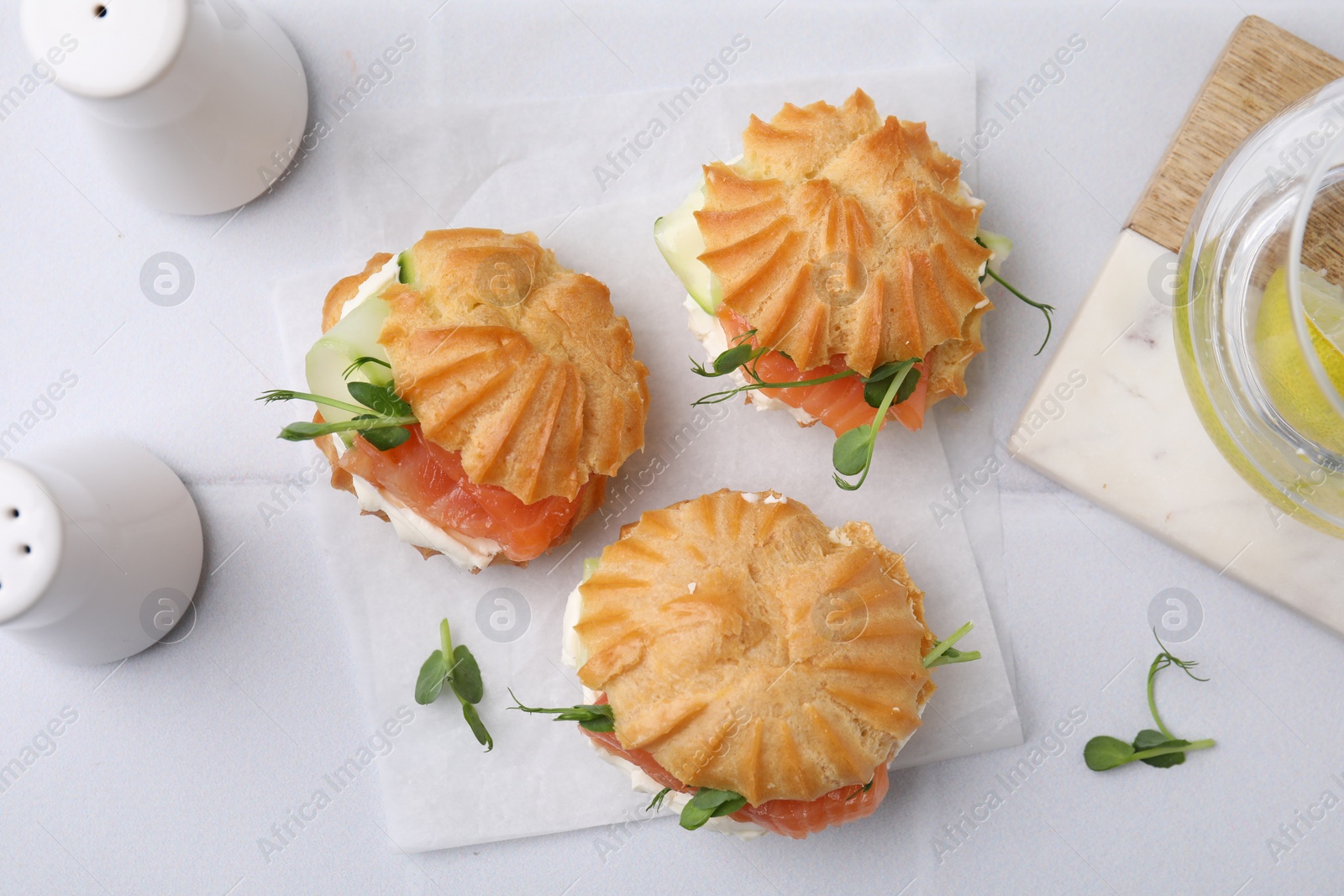 Photo of Delicious profiteroles with cream cheese and salmon on white tiled table, flat lay