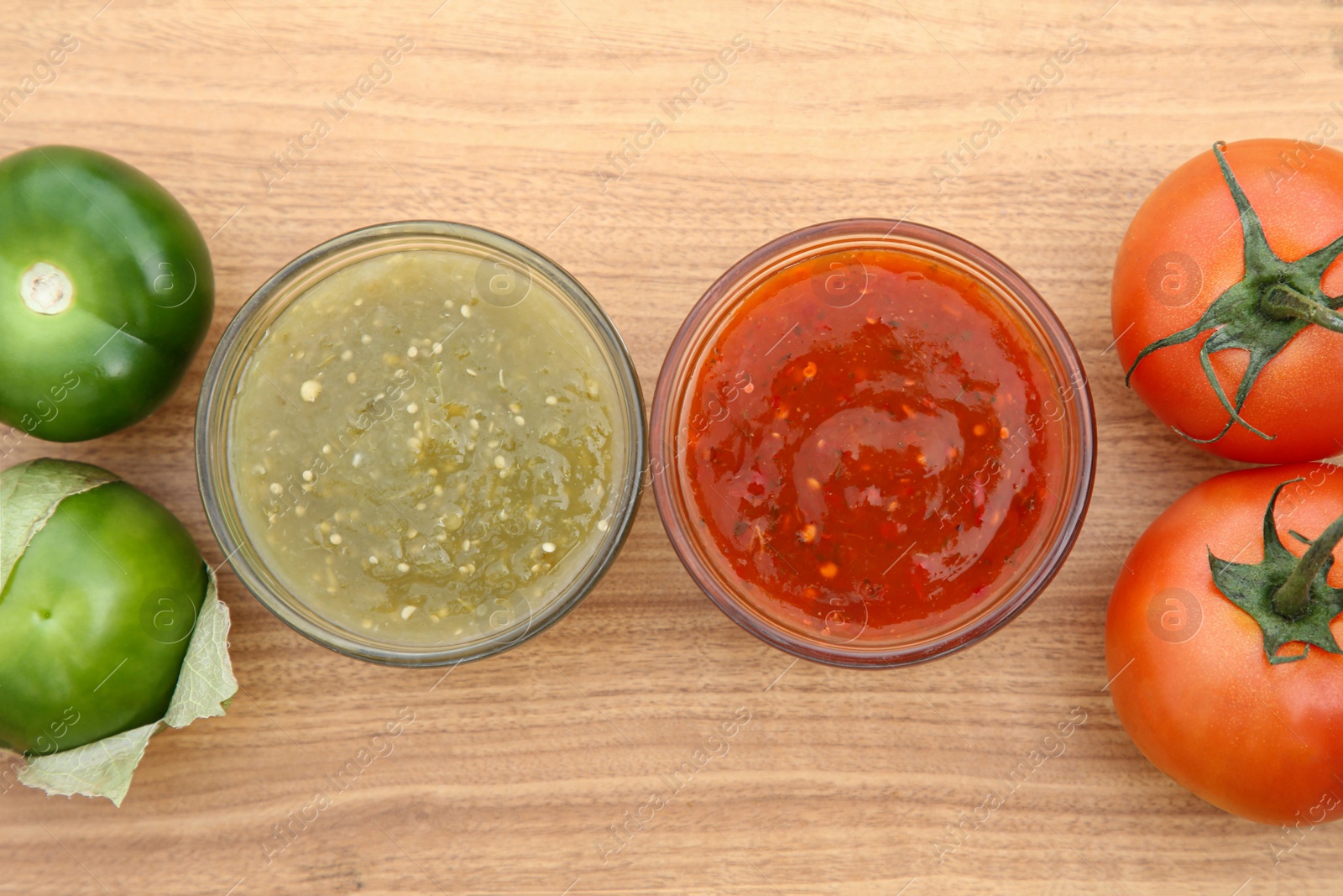 Photo of Tasty salsa sauces and different tomatoes on wooden table, flat lay