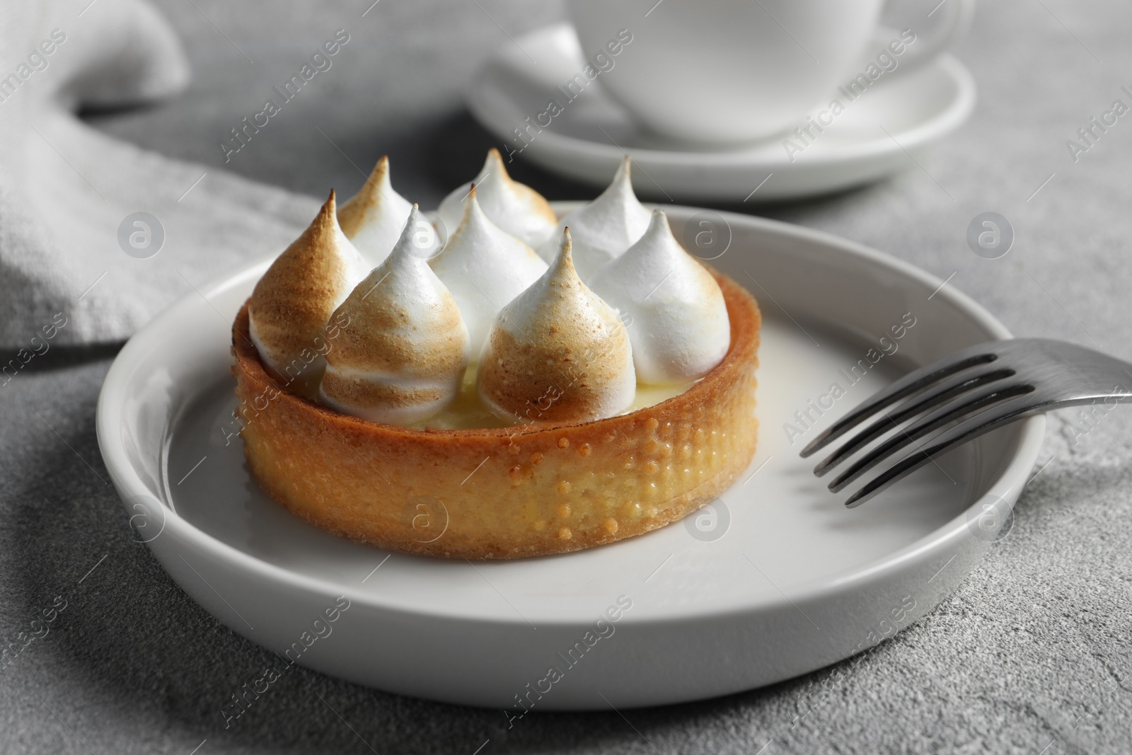 Photo of Tartlet with meringue served on light grey table, closeup. Tasty dessert