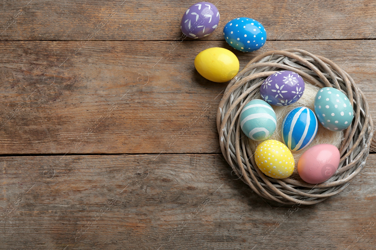 Photo of Wicker nest with painted Easter eggs on wooden table, top view. Space for text