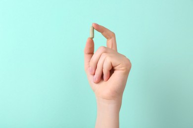 Woman holding vitamin capsule on turquoise background, closeup