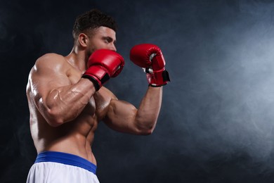 Photo of Man wearing boxing gloves fighting in smoke on black background, low angle view. Space for text