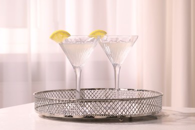 Tray with martini glasses of fresh cocktail and lemon slices on white table indoors