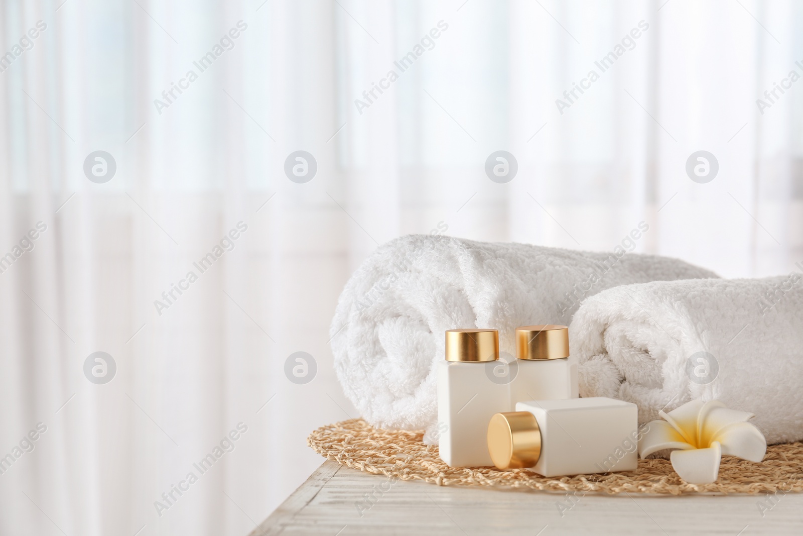 Photo of Cosmetic bottles, flower and towels on white wooden table indoors, space for text. Spa treatment