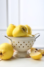 Photo of Tasty ripe quinces and metal colander on white wooden table