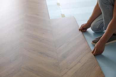 Photo of Worker installing laminated wooden floor indoors, closeup