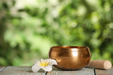 Golden singing bowl, mallet and flower on wooden table outdoors