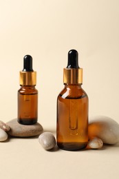 Bottles of cosmetic serum and stones on beige background