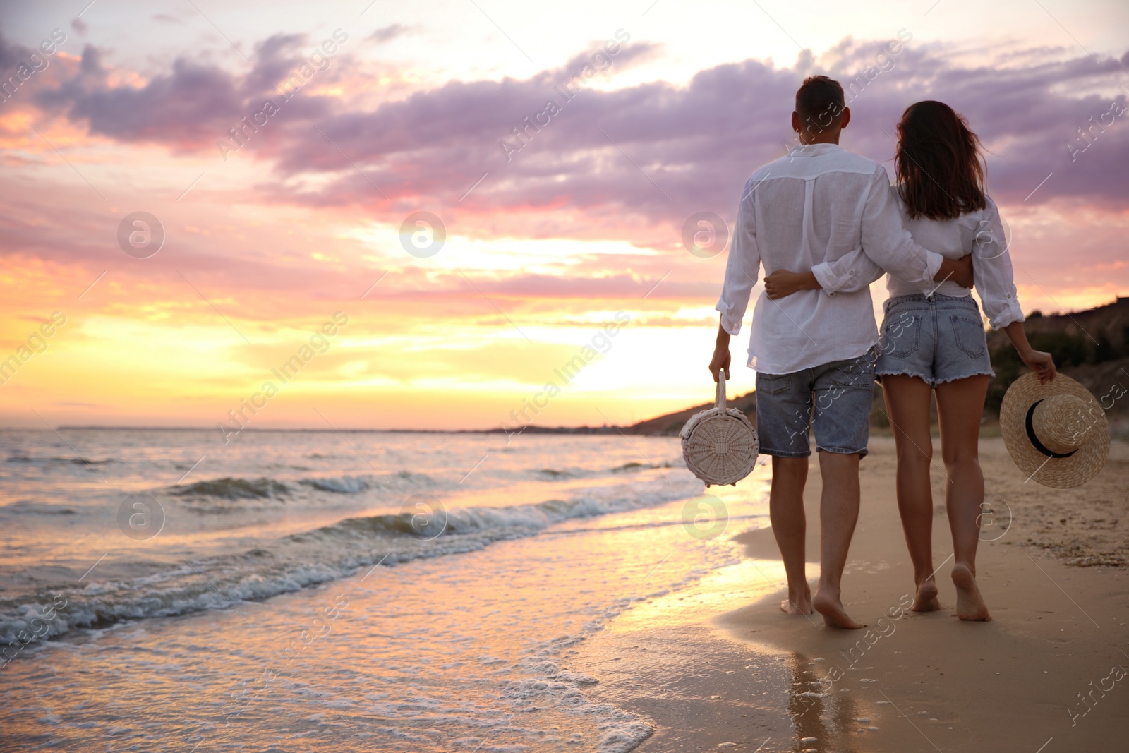 Photo of Lovely couple walking on beach at sunset, back view. Space for text