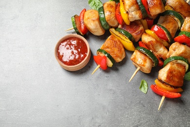 Photo of Delicious chicken shish kebabs with vegetables and ketchup on grey table. Space for text
