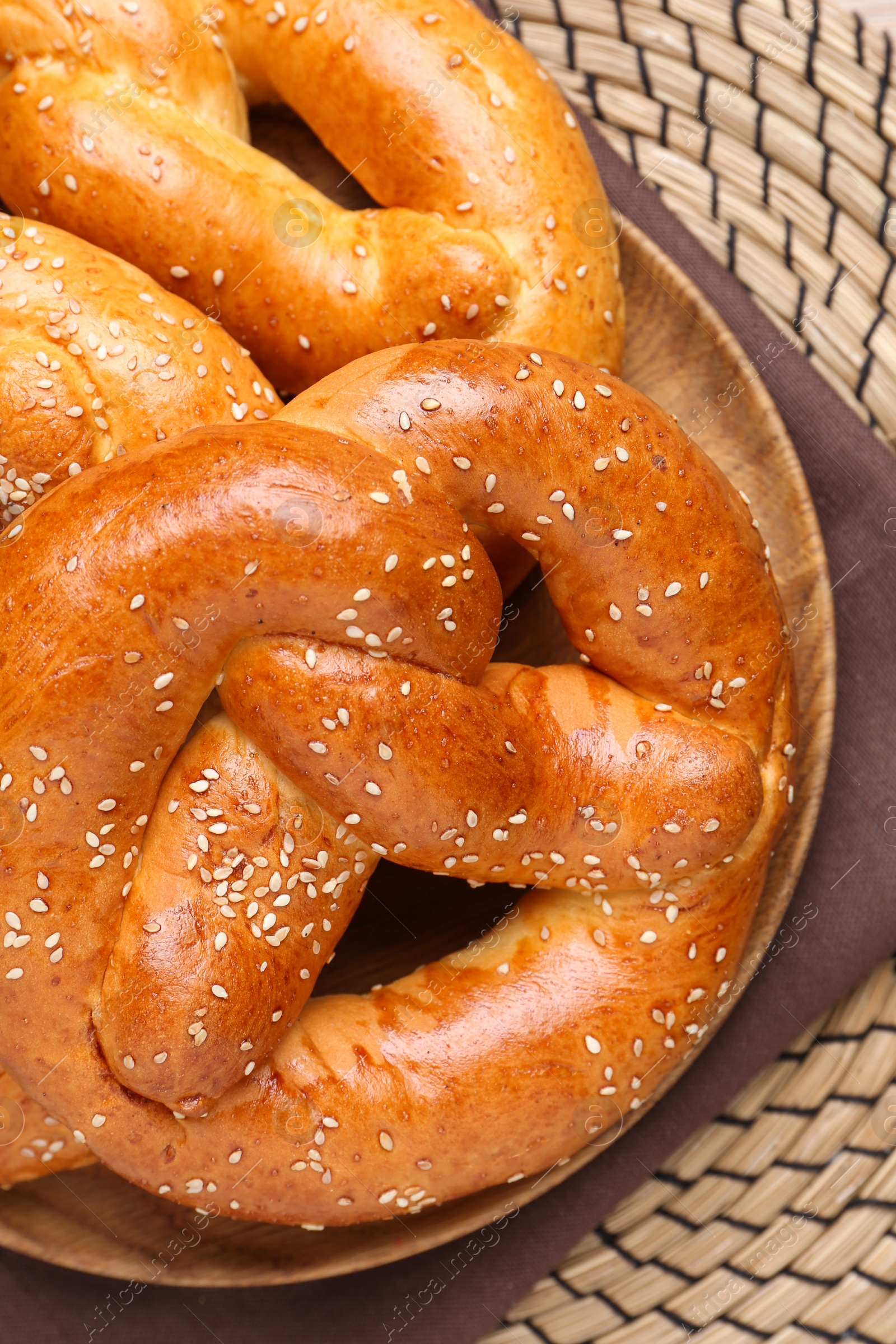 Photo of Delicious pretzels with sesame seeds on wicker mat, top view