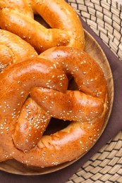 Delicious pretzels with sesame seeds on wicker mat, top view