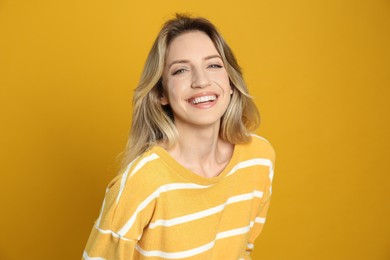 Portrait of happy young woman with beautiful blonde hair and charming smile on yellow background