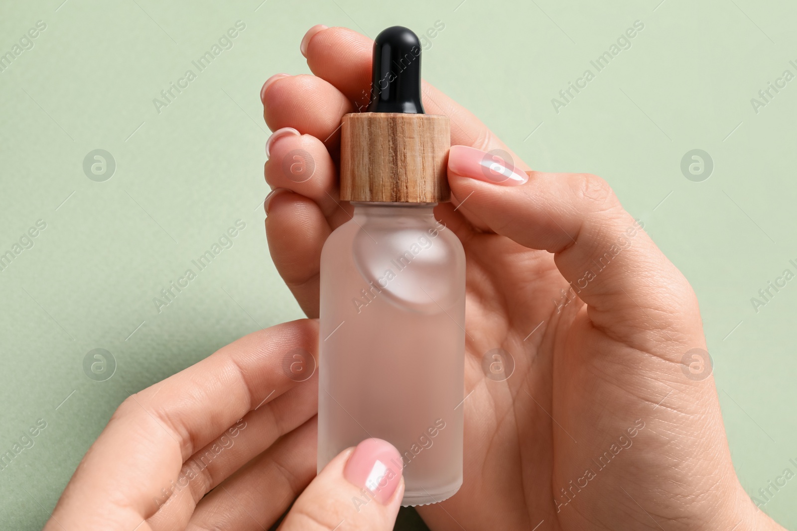 Photo of Woman holding bottle with serum against olive background, closeup