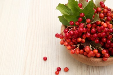 Photo of Bowl with tasty viburnum berries on white wooden table. Space for text