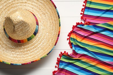 Mexican sombrero hat and colorful poncho on white wooden background, flat lay