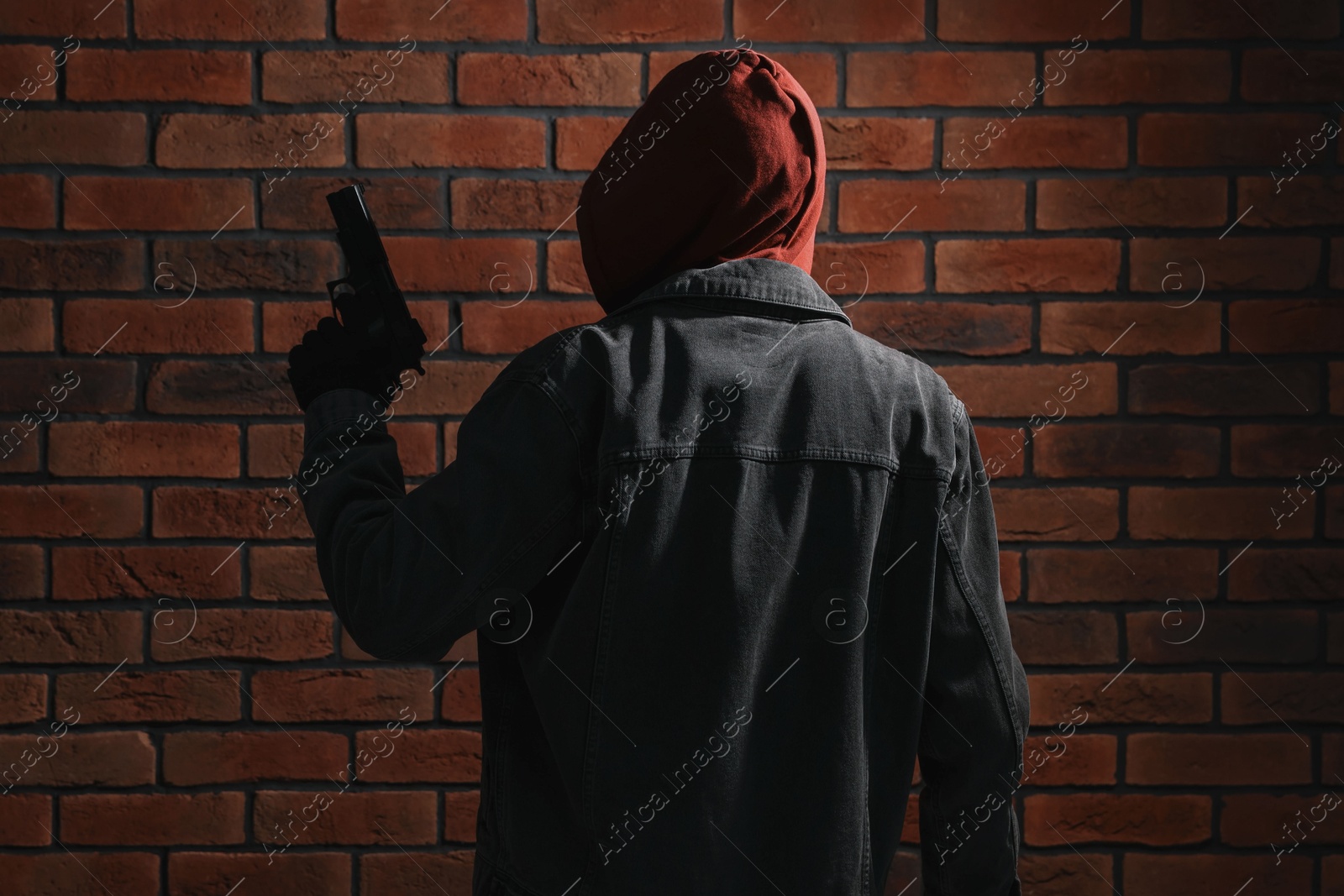 Photo of Thief in hoodie with gun against red brick wall, back view