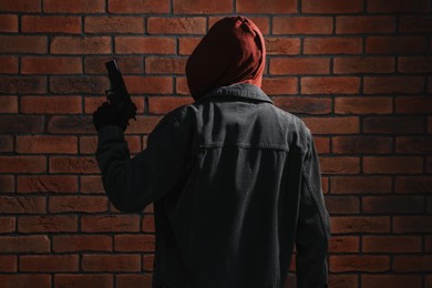 Photo of Thief in hoodie with gun against red brick wall, back view