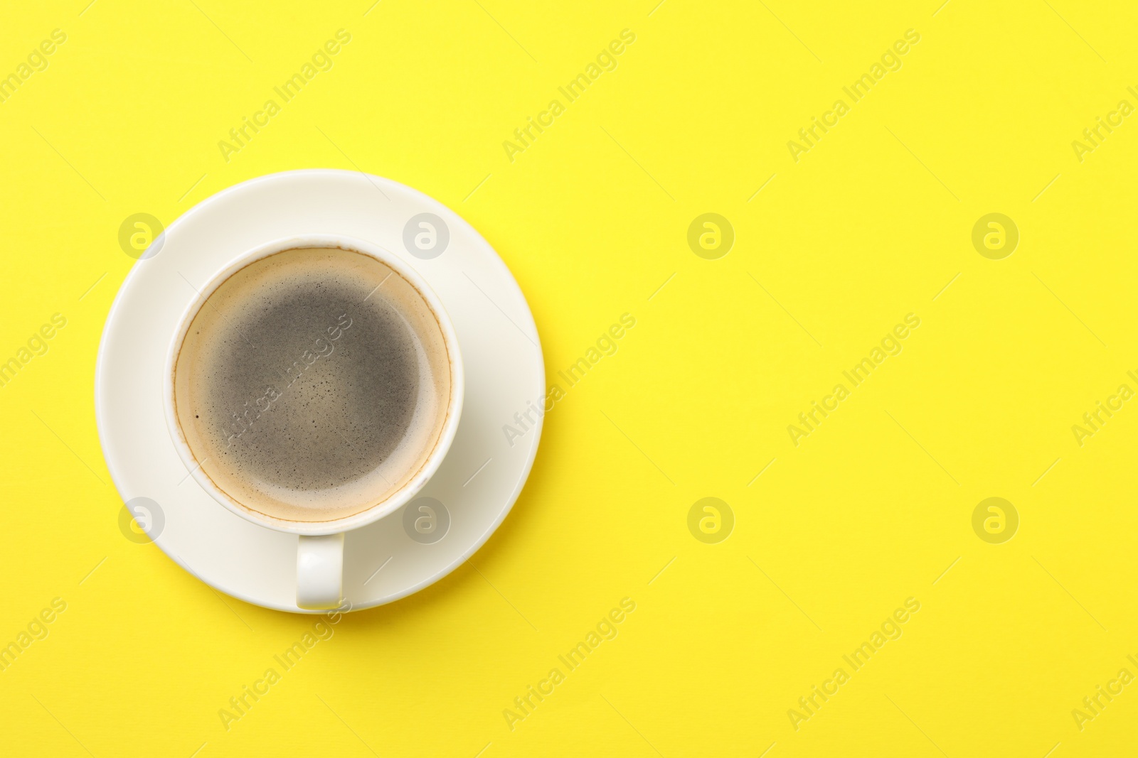 Photo of Aromatic coffee in cup on yellow background, top view. Space for text