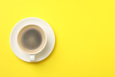 Photo of Aromatic coffee in cup on yellow background, top view. Space for text