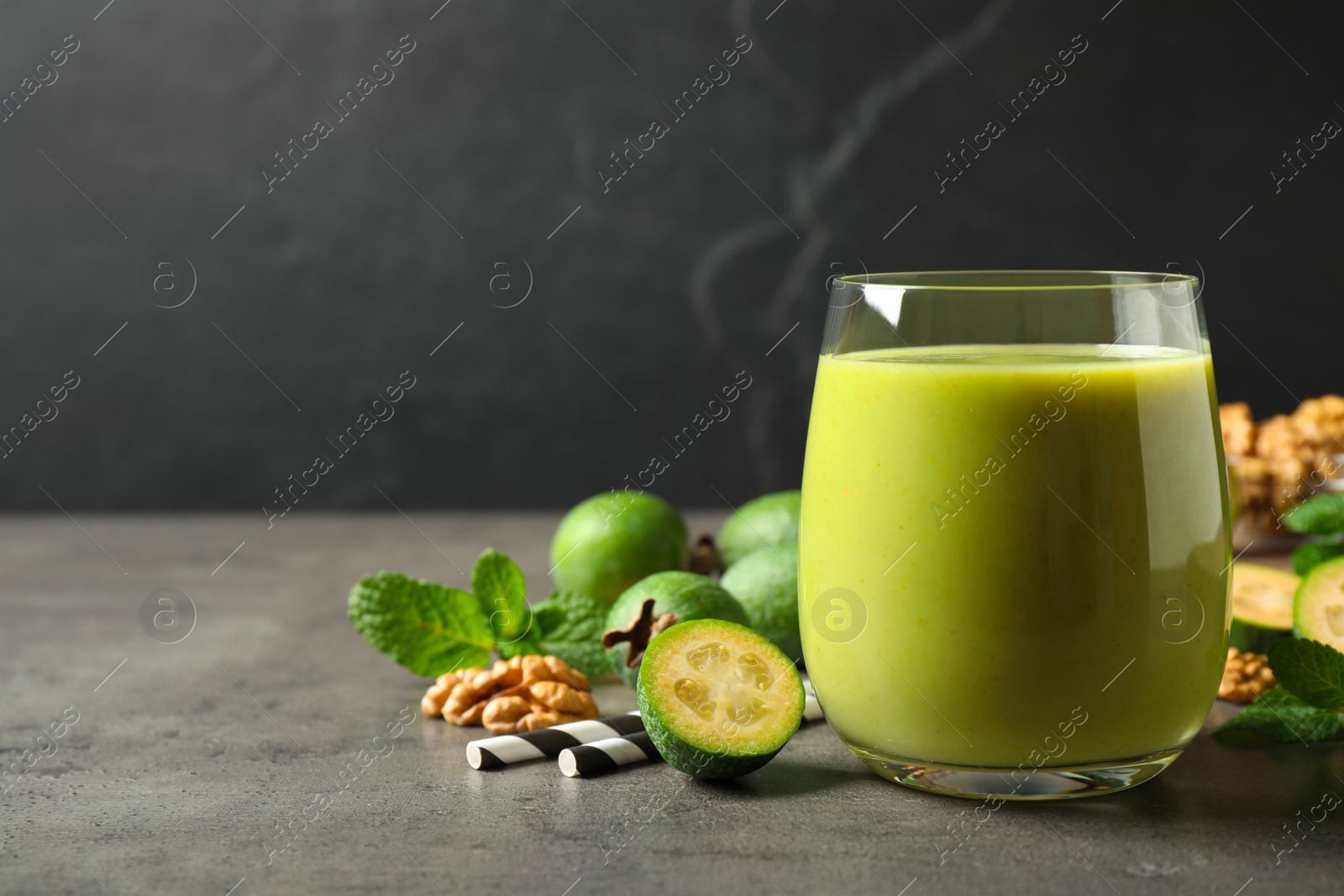 Photo of Fresh feijoa smoothie in glass on grey table, space for text