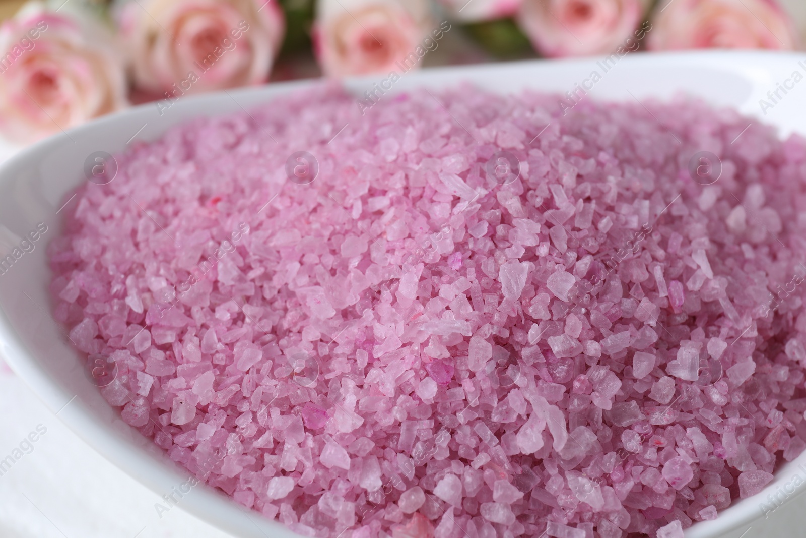Photo of Bowl with pink sea salt on blurred background, closeup