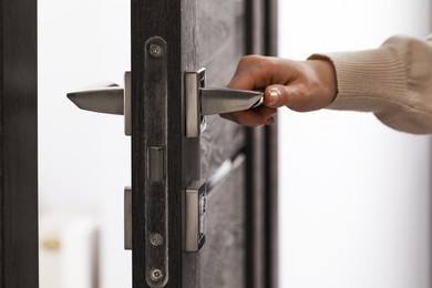 Photo of Woman opening wooden door indoors, closeup of hand on handle