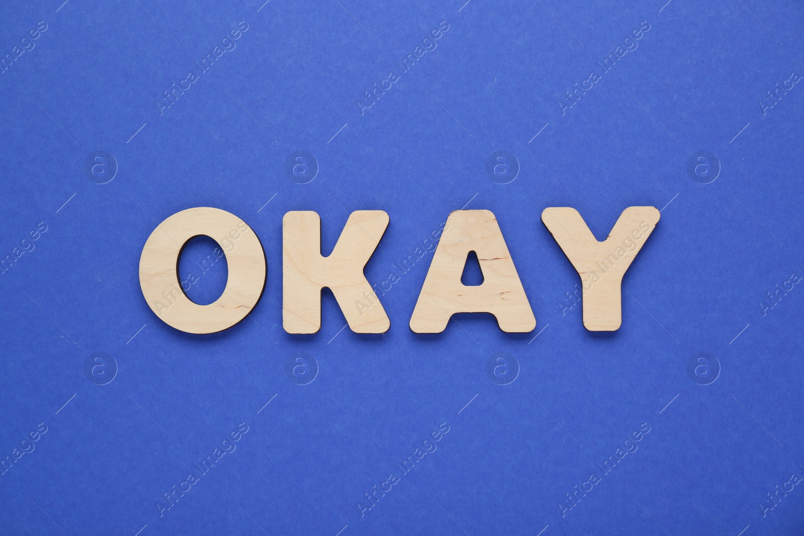 Photo of Word Okay made of wooden letters on blue background, top view