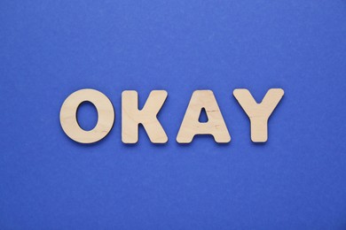 Photo of Word Okay made of wooden letters on blue background, top view