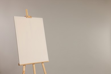 Wooden easel with blank canvas on grey background. Space for text