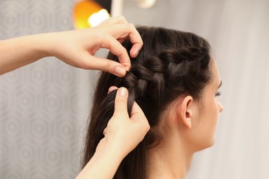 Photo of Professional stylist braiding client's hair on blurred background