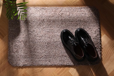 Stylish door mat with shoes on floor, top view